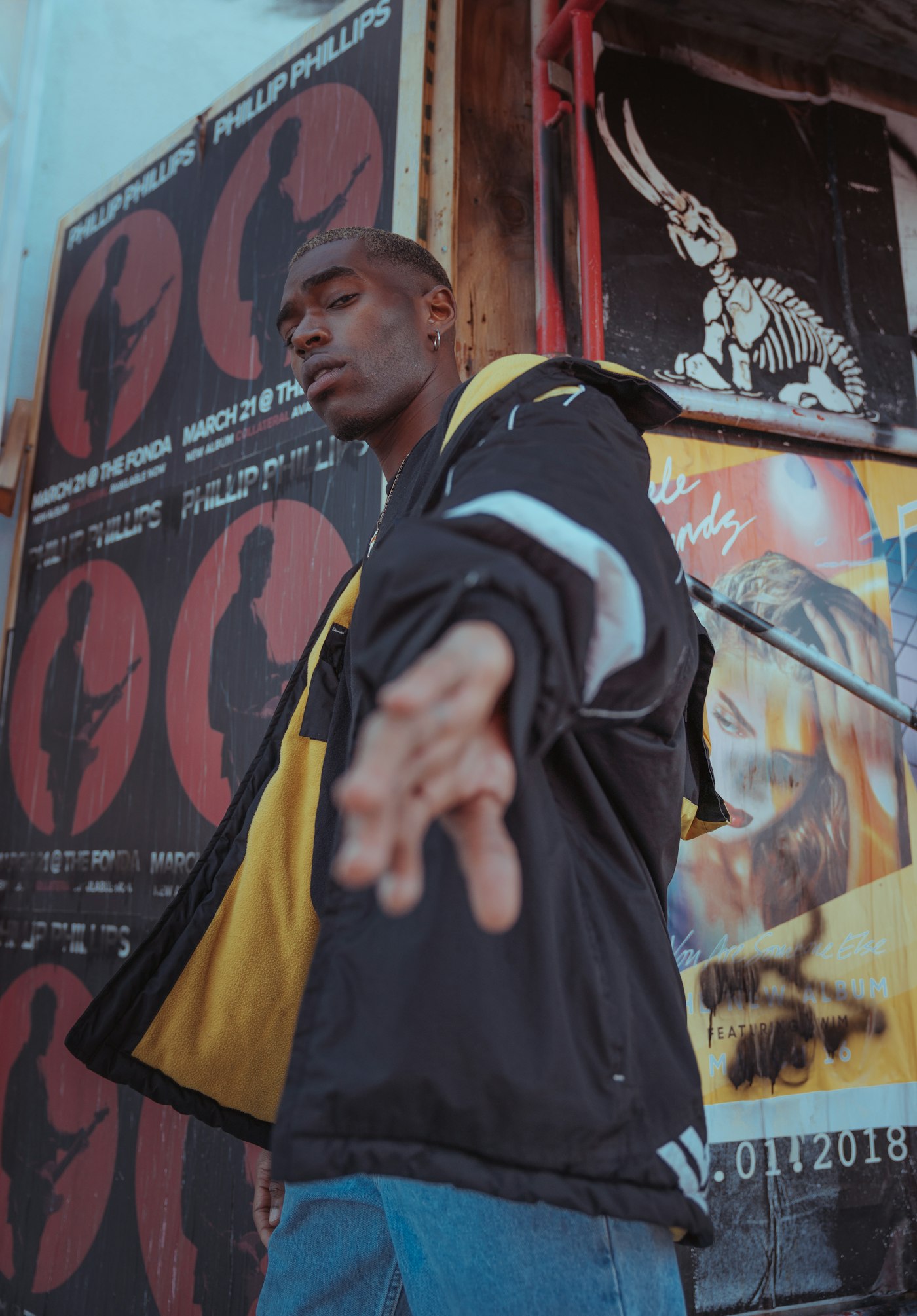 Model in an oversized black and yellow jacket reaching toward the camera